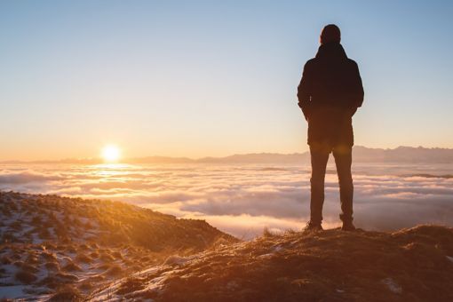 Man standing on mountain peak watching sunset