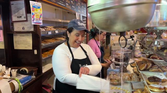 Employees stand behind the counter of Rudy's Pastry Shop and fulfill orders. 