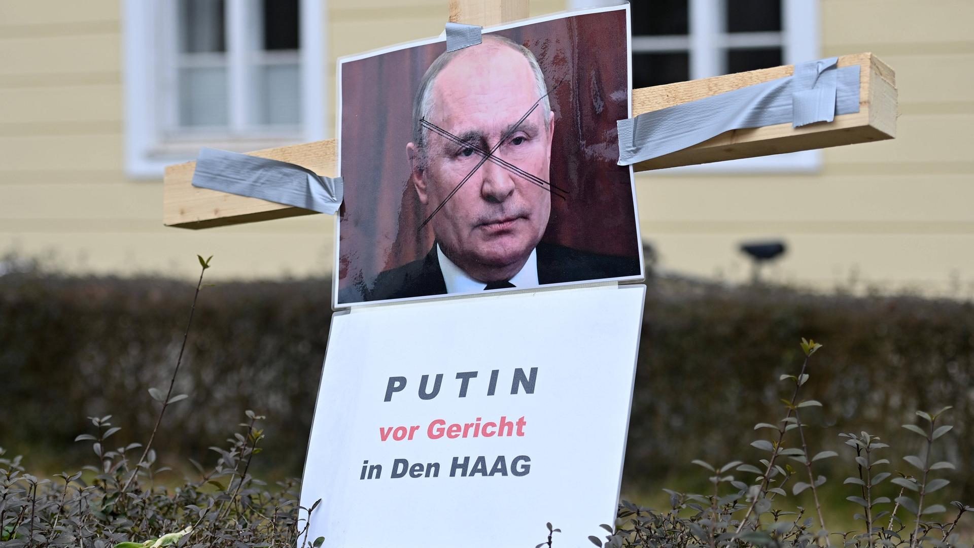 Protestaktion gegen Wladimir Putin und Russland gegen Krieg und Einmarsch seiner Truppen in die Ukraine am am Europaplatz in München neben dem Generalskonsulat der Russischen Föderation am 02.03.20222. An einem Holzkreuz haengt ein Portraet von Wladimir Putin und die Forderung:PUTIN VOR GERICHT IN DEN HAAG.