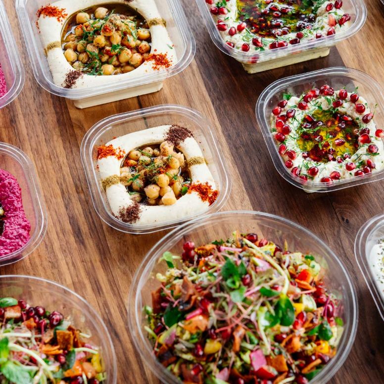 A selection of Syrian dishes sitting in to go plates on a wooden table