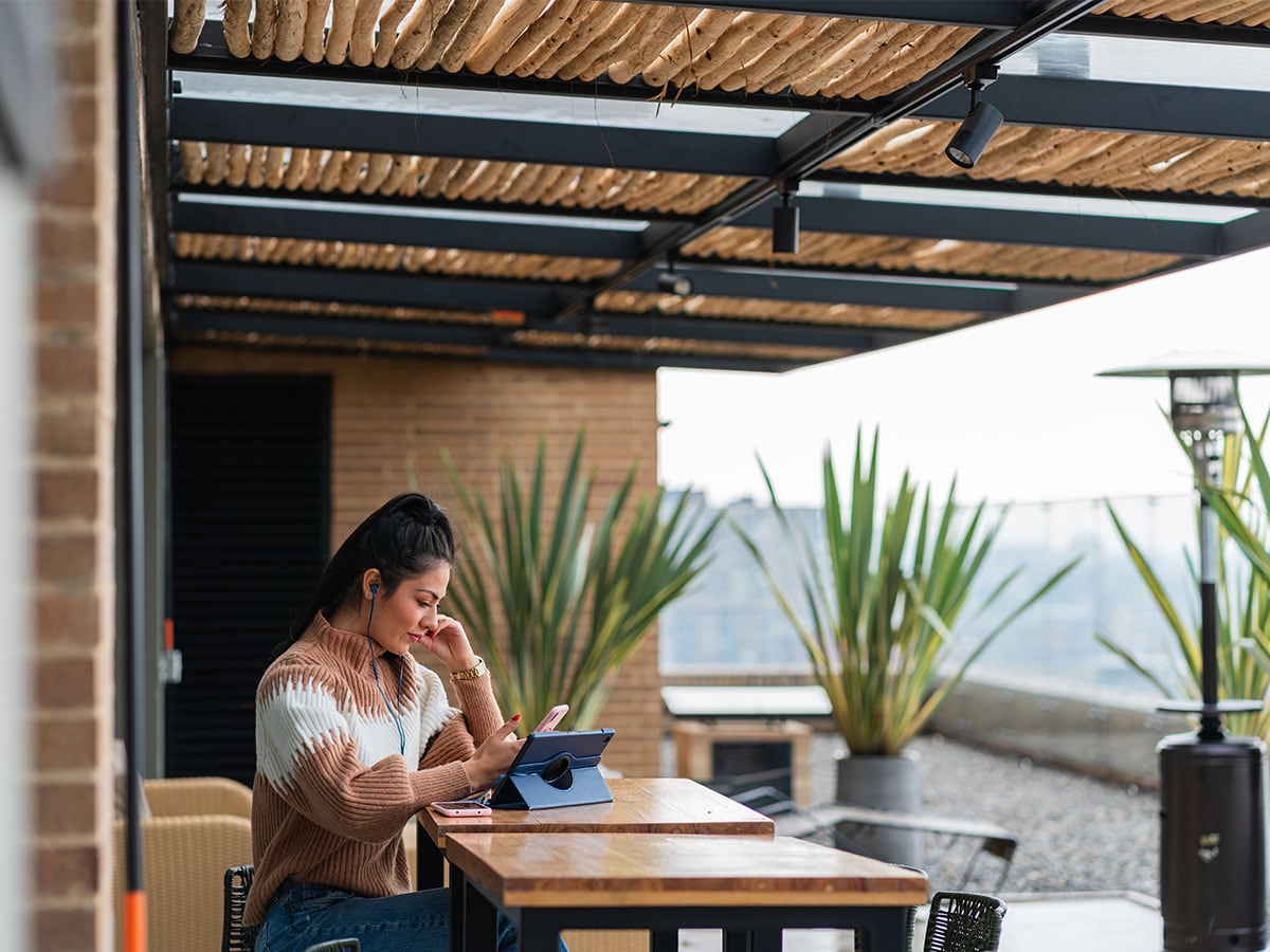 mulher sentada à mesa de pátio com smartphone e tablet