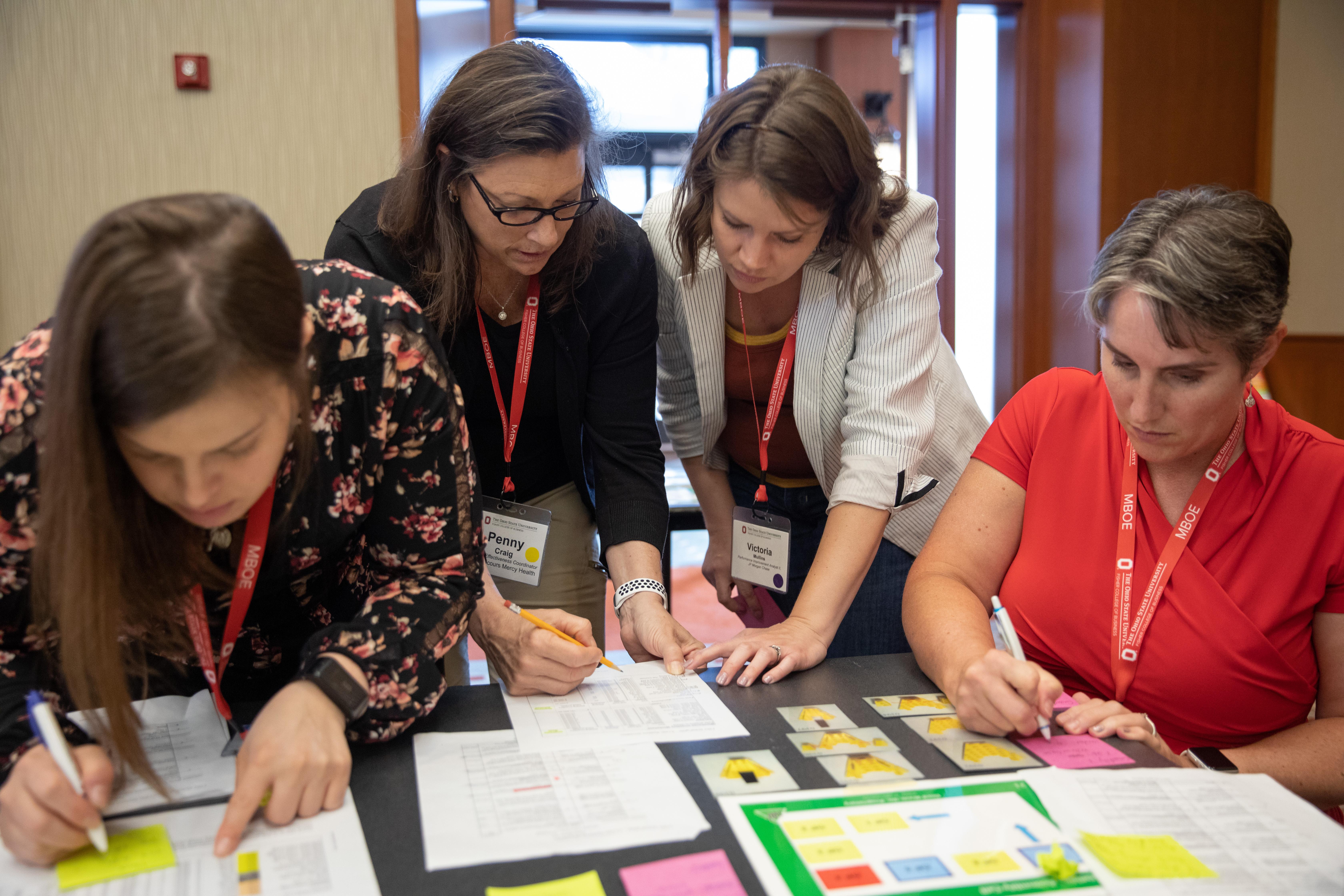 Four women standing over a table discussing documents displayed on the table