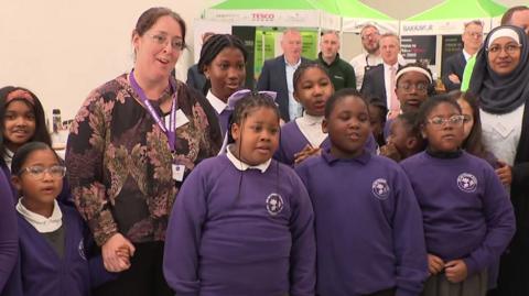 A group of schoolchildren in purple jumpers singing Happy Birthday to King Charles