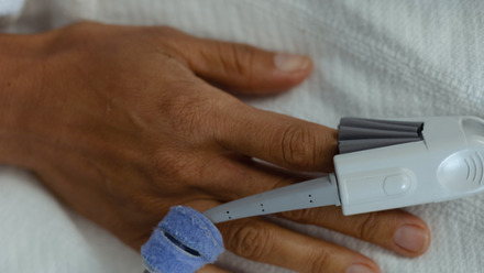 A hand with a pulse oximeter connected to the index finger.