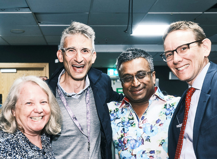 One woman and three men standing together in a backstage environment and smiling for the camera