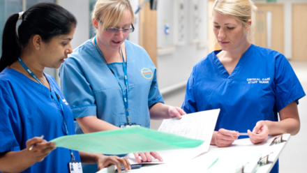 Three women in blue scrubs discussing a file