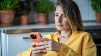 Serious woman holding smartphone attentive reading received message sitting at home with houseplants Pensive millennial 