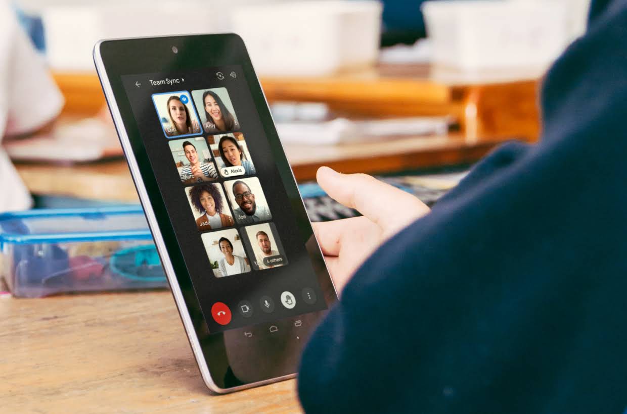 Een hand op een tafel die een tablet vasthoudt met daarop een Google Meet-gesprek.