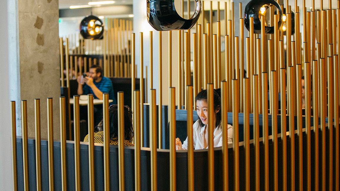 Two women sitting in a cafe at a booth lined with tall, verticle metal rods.