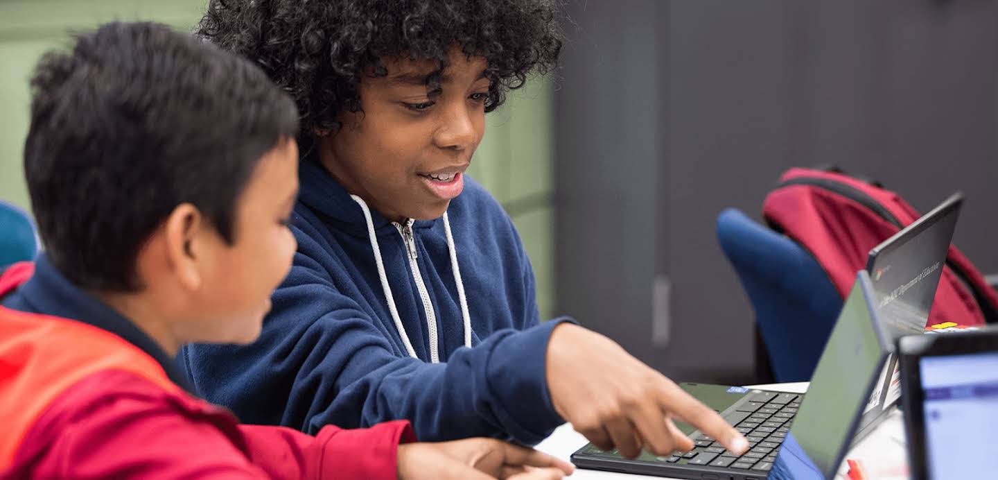 Dua siswa menggunakan Chromebook mereka di sekolah.