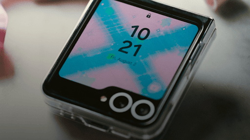 A folded flip phone screen with an abstract blue X and pink wallpaper that shows the time and date.