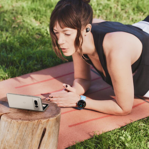 A person exercising on a yoga mat wearing a Wears OS smartwatch and earbuds, and looking at a foldable Android phone.