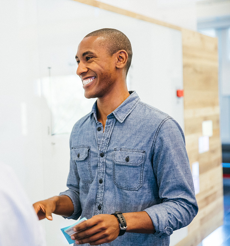 A man smiling as he stands near a whiteboard.