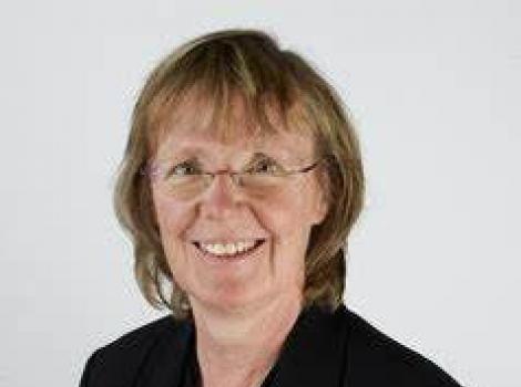 Head shot of a woman with short blonde hair, glasses, and a black shirt.