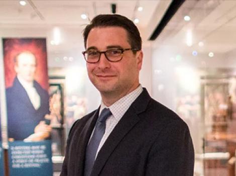 bust length photo of a man wearing glasses and wearing a suit in an exhibition space