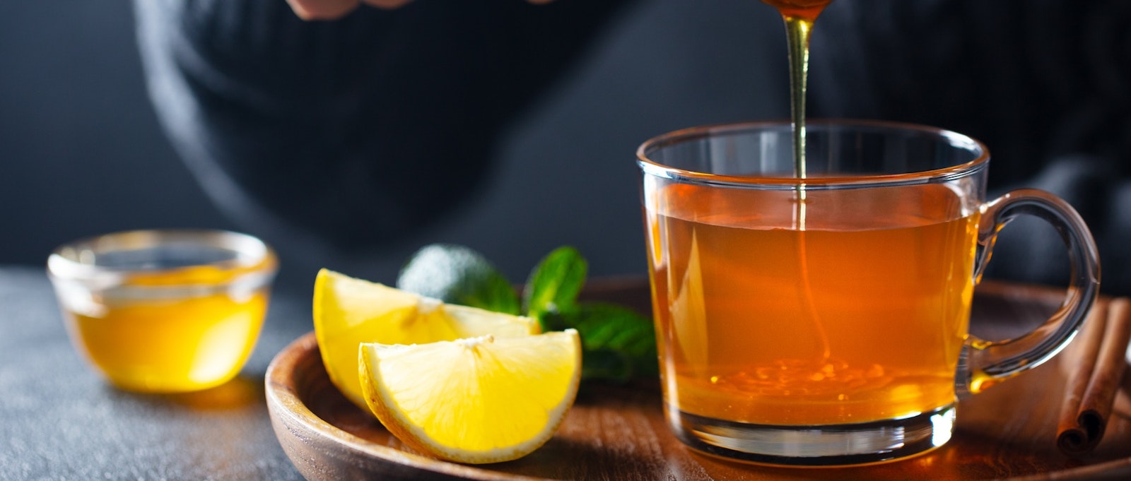 Cup of tea with pouring honey and lemon. Grey background.