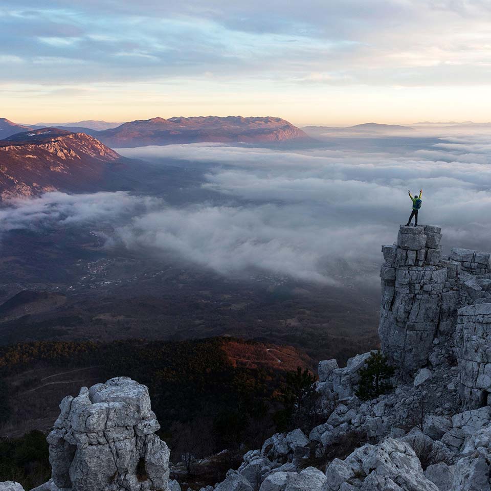 Man and woman standing on rock formation wit the beautiful panorama of Vipava valley in Slovenia,at sunset, looking from the top of Caven mountain