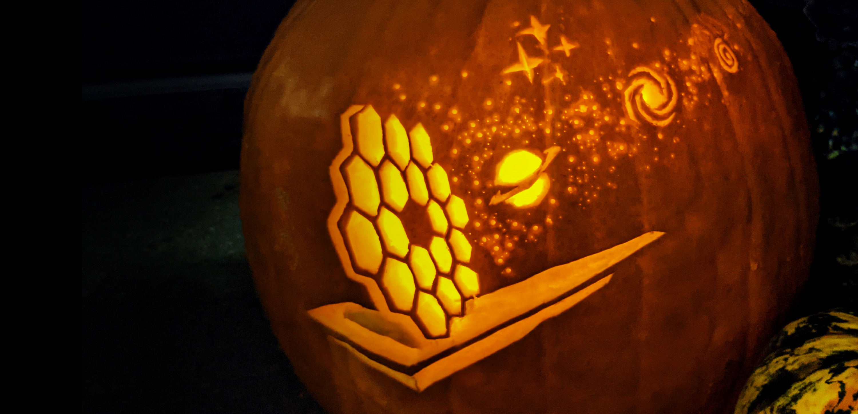 A pumpkin carved with the Webb telescope "looking at stars, planets, galaxies all glowing as they are backlit fromthe light within the pumpkin.