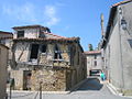 Une rue avec maison à encorbellement menaçant de s'écrouler (le clocher de l'église apparaît à droite, le château dans le fond)