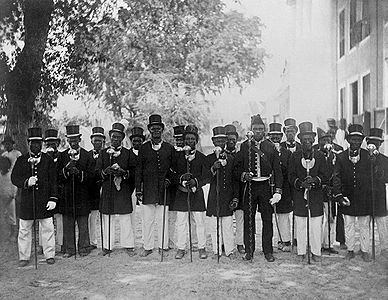 Granman Jankoeso of the Saramkaner Maroon with his captains in the garden of the "Gouvernementsgebouw" in Paramaribo. This picture has been restored in anticipation of a collection by the Royal Institute for the Tropics / Tropenmuseum. This picture is now officially uploaded in a low resolution [File:Tropenmuseum Royal Tropical Institute Objectnumber 60008914 Granman Jankoeso van de Saramakanersp.jpg here]. This represents the practice where pictures may be provided to us in a high resolution when we are willing to restore them..