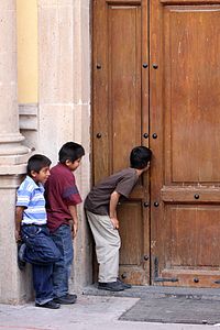 Boys peeping though a church door in Mexico