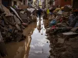 A person walks through a street with piled furniture and rubbish on the sides in an area affected by floods in Paiporta, Valencia, Spain, Tuesday, Nov. 5, 2024. (AP Photo/Emilio Morenatti)