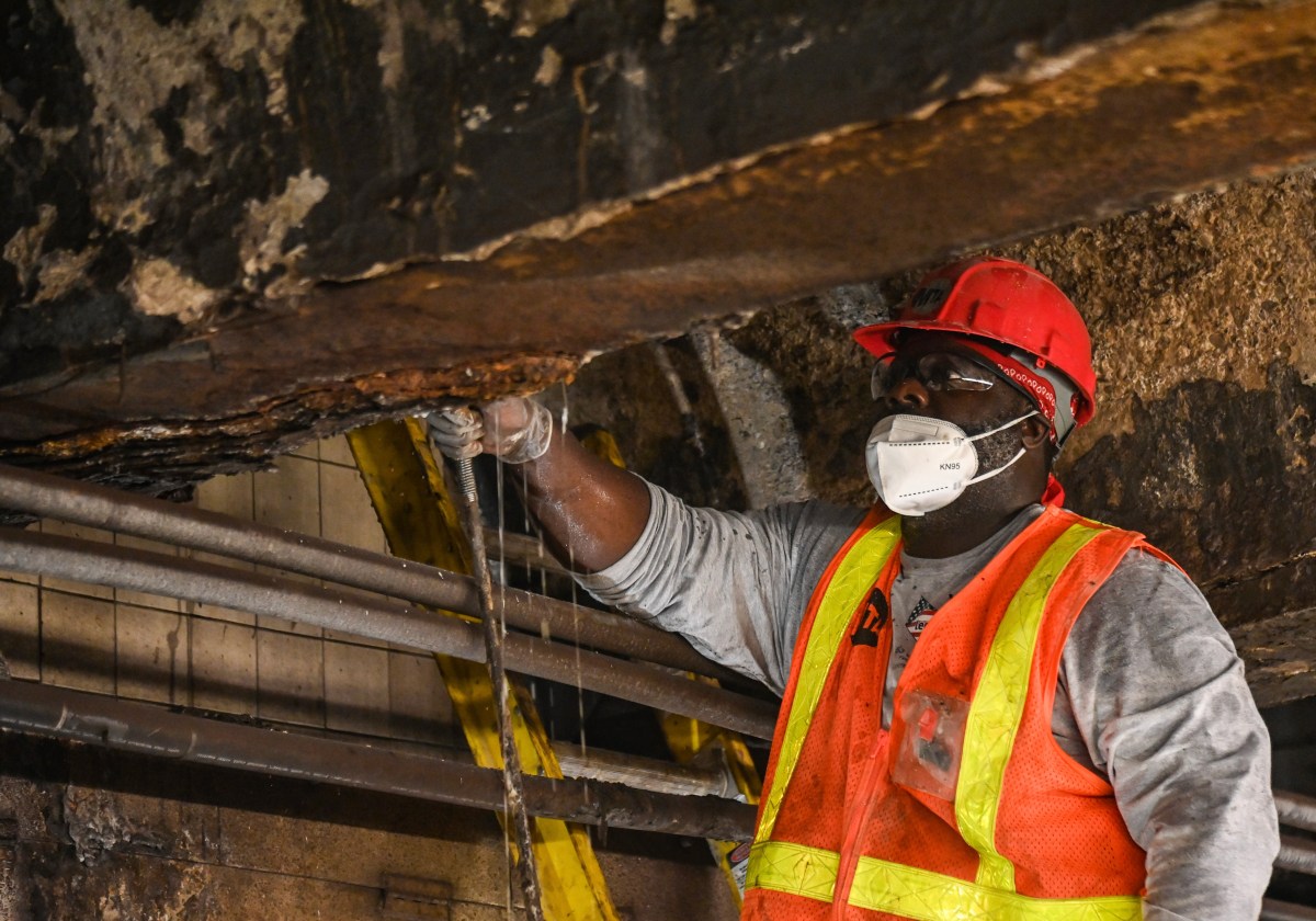 MTA worker removing rust from overhead beams at subway station