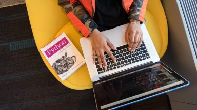 women coding on laptop with python book