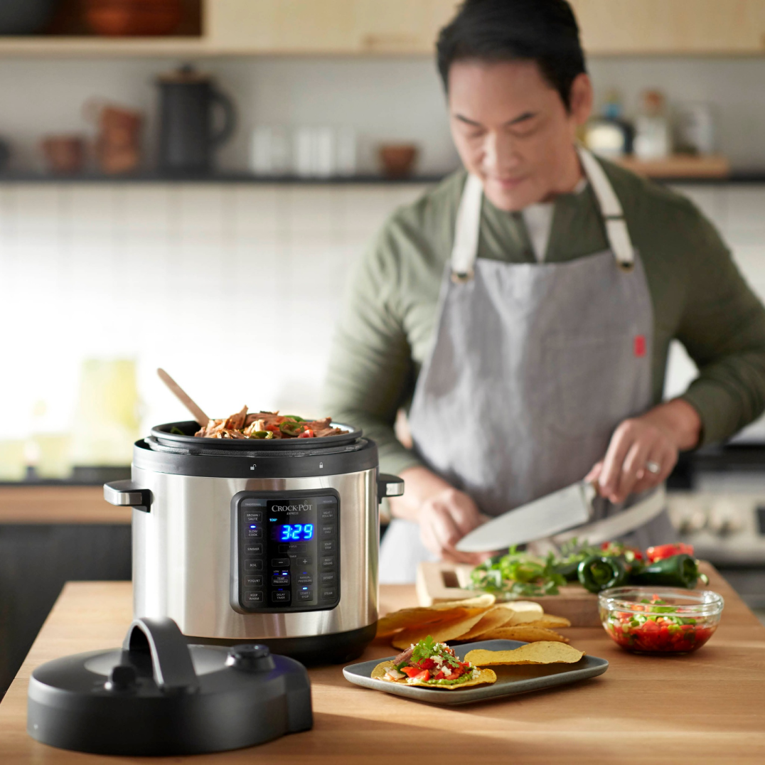 A chef wearing an apron cooking in the kitchen with a using smart crock pot device in the foreground.