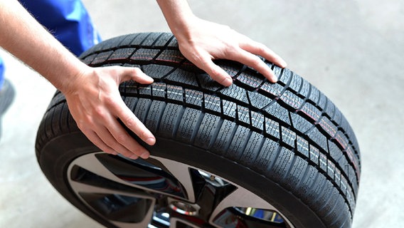 Ein Mitarbeiter einer KFZ-Werkstatt hält einen Reifen mit Felge in den Händen. © Fotolia.com Foto: industrieblick