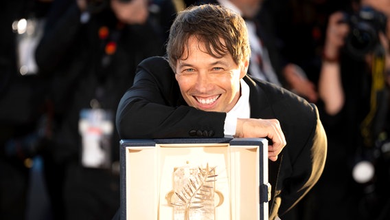 Der Regisseur Sean Baker lächelt glücklich mit seiner Goldenen Palme für den Film "Anora" ©  Scott A Garfitt/Invision/AP/dpa +++ dpa-Bildfunk +++ Foto: Scott A Garfitt