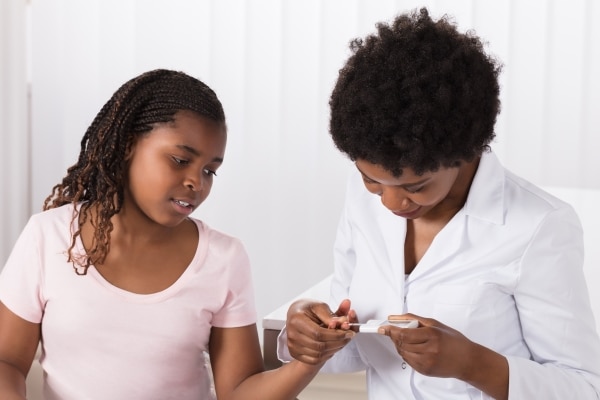 A doctor uses a glucometer to check a young patient’s glucose level in a hospital examination room.