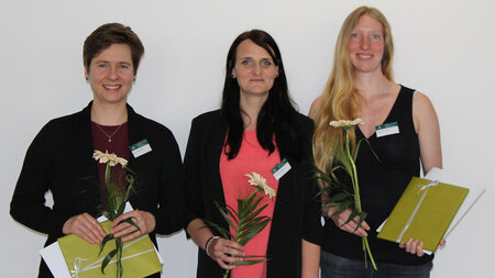 Drei FRauen stehen nebeneinander und halten Umschläge und Blumen in ihren Händen.