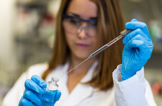 Female scientist in a lab coat takes from a small glass with a pipette